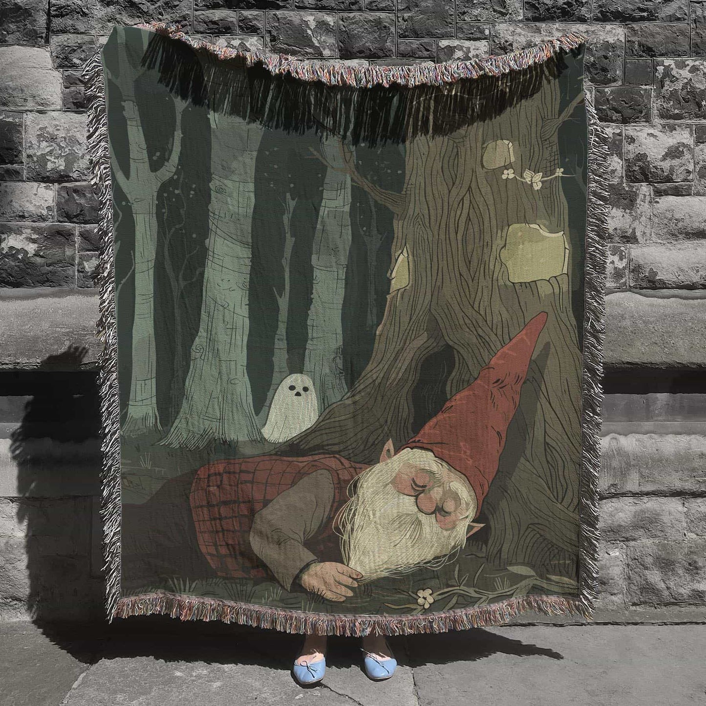Woven cotton blanket depicting a sleeping gnome under a large tree, with a small ghost-like forest spirit in the background surrounded by dark green woods.