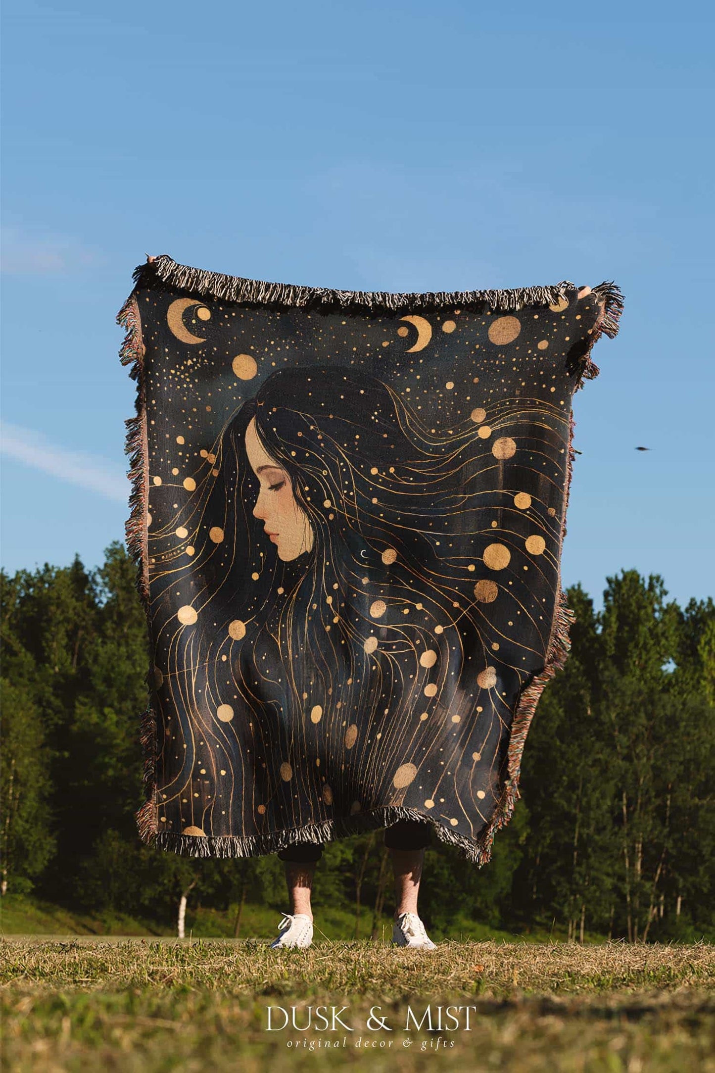 Woven cotton blanket featuring a profile of a woman with flowing hair illustrated as starry constellations, accented with golden moons and celestial motifs on a dark background.