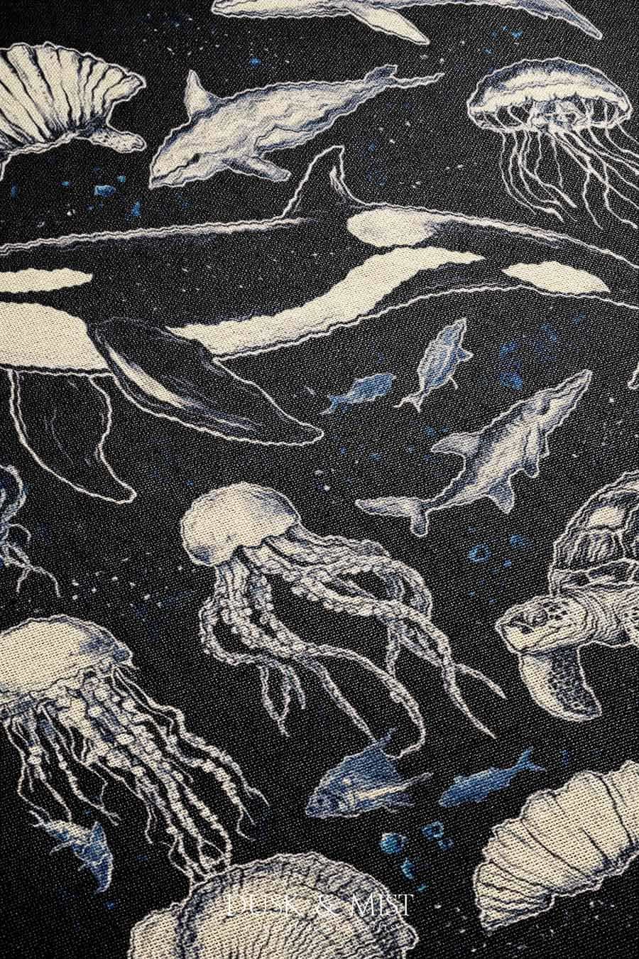 Woven cotton blanket featuring detailed marine life illustration — orca, dolphins, sea turtle, octopus, jellyfish, seashells, and fish on a black background.