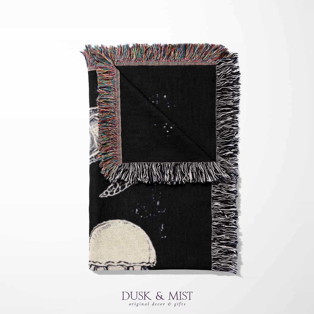 Woven cotton blanket featuring detailed ocean life illustration — whales, orca, turtles, jellyfish, octopus, seashells, fish, and coral on a black background.