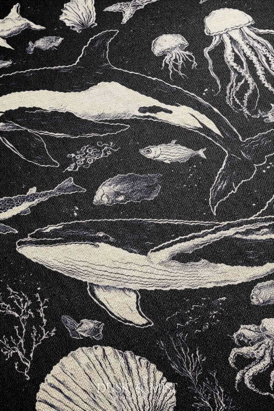 Woven cotton blanket featuring detailed ocean life illustration — whales, orca, turtles, jellyfish, octopus, seashells, fish, and coral on a black background.