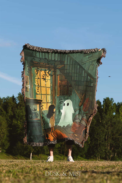 Woven cotton blanket depicting a small ghost and a young girl standing in a warmly lit wooden room filled with plants, books, and soft evening light streaming through a door.