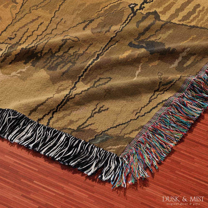 Woven cotton blanket featuring a small ghost standing in a golden meadow facing a brown and white cow, with a rustic cabin and forested hills in the background.