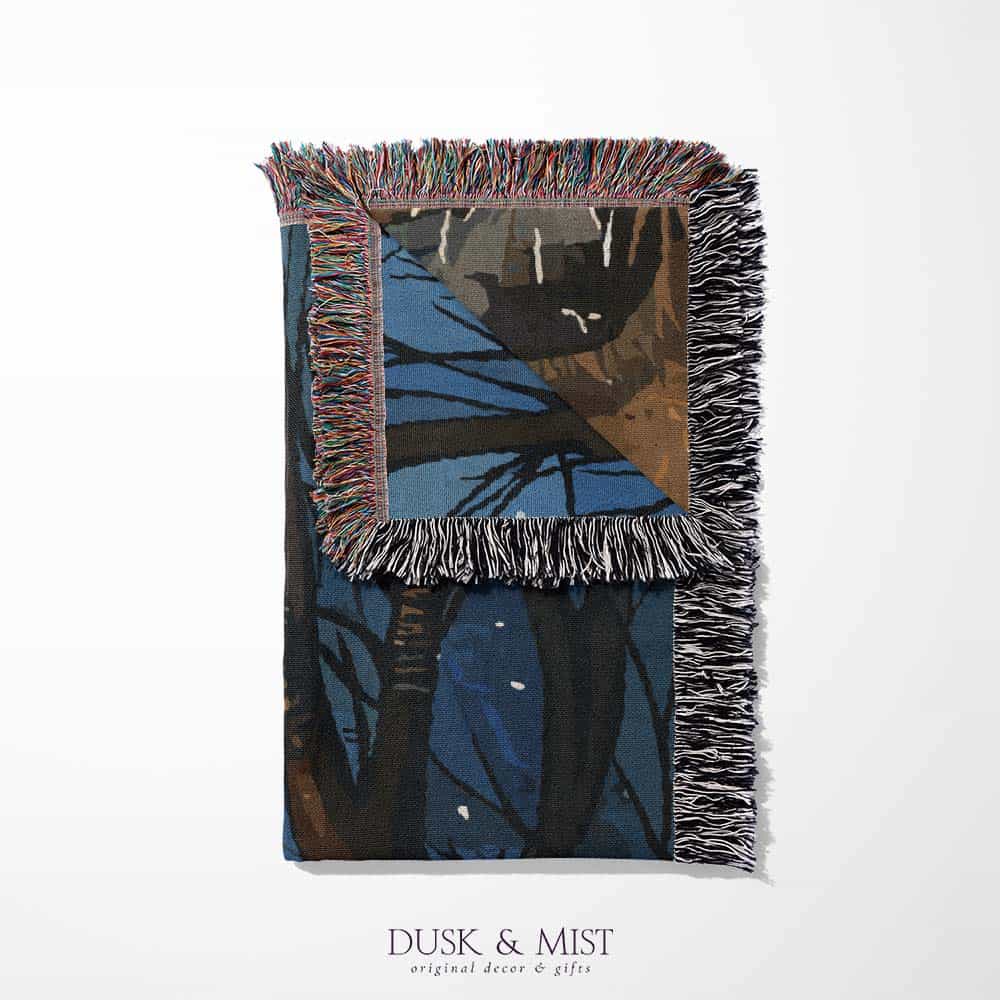 Woven cotton blanket featuring a witch and a ghost sitting by a campfire under a crescent moon in a dark forest setting.