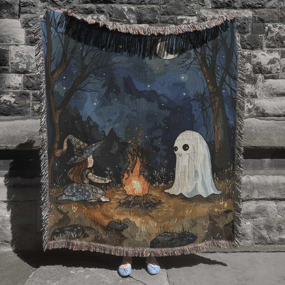 Woven cotton blanket featuring a witch and a ghost sitting by a campfire under a crescent moon in a dark forest setting.