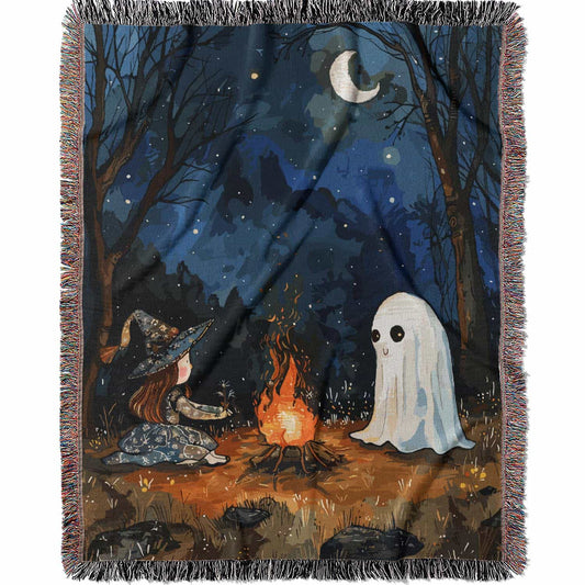 Woven cotton blanket featuring a witch and a ghost sitting by a campfire under a crescent moon in a dark forest setting.