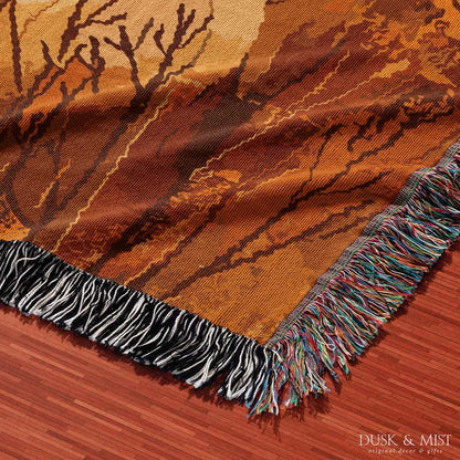 Woven cotton blanket showing a small ghost holding a basket, surrounded by pumpkins and autumn foliage in warm golden and orange tones.