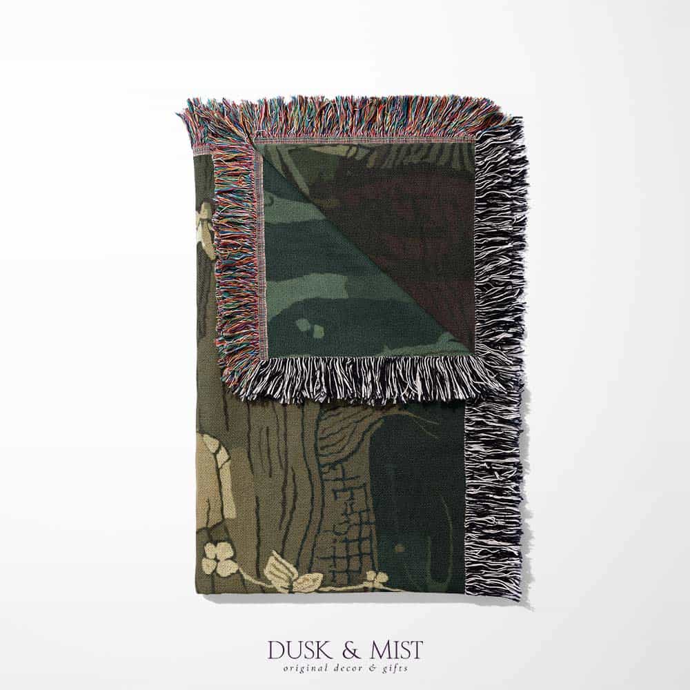 Woven cotton blanket depicting a sleeping gnome under a large tree, with a small ghost-like forest spirit in the background surrounded by dark green woods.