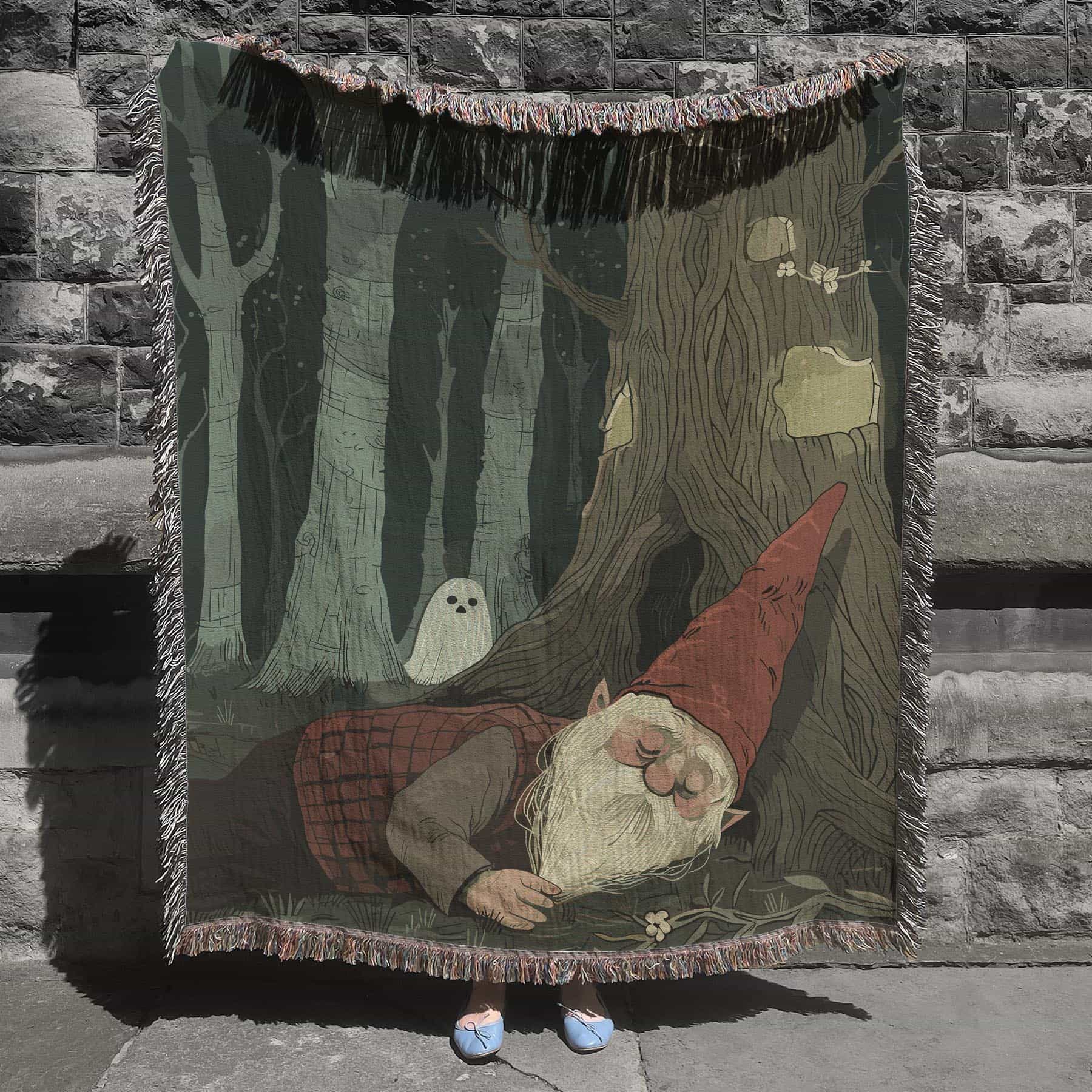 Woven cotton blanket depicting a sleeping gnome under a large tree, with a small ghost-like forest spirit in the background surrounded by dark green woods.