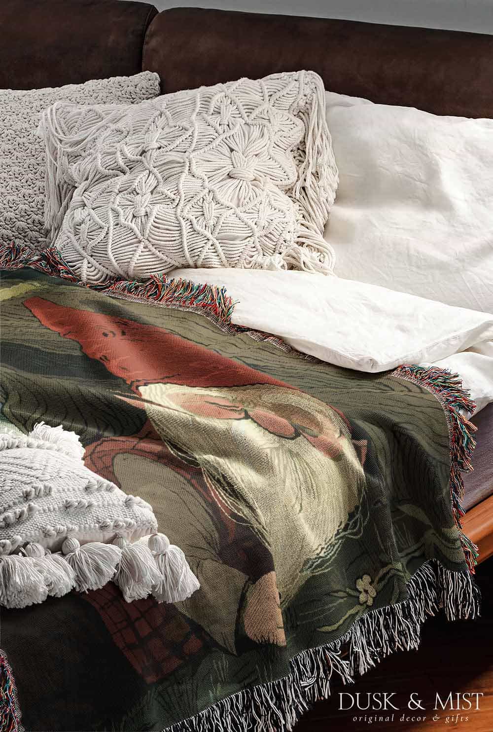 Woven cotton blanket depicting a sleeping gnome under a large tree, with a small ghost-like forest spirit in the background surrounded by dark green woods.