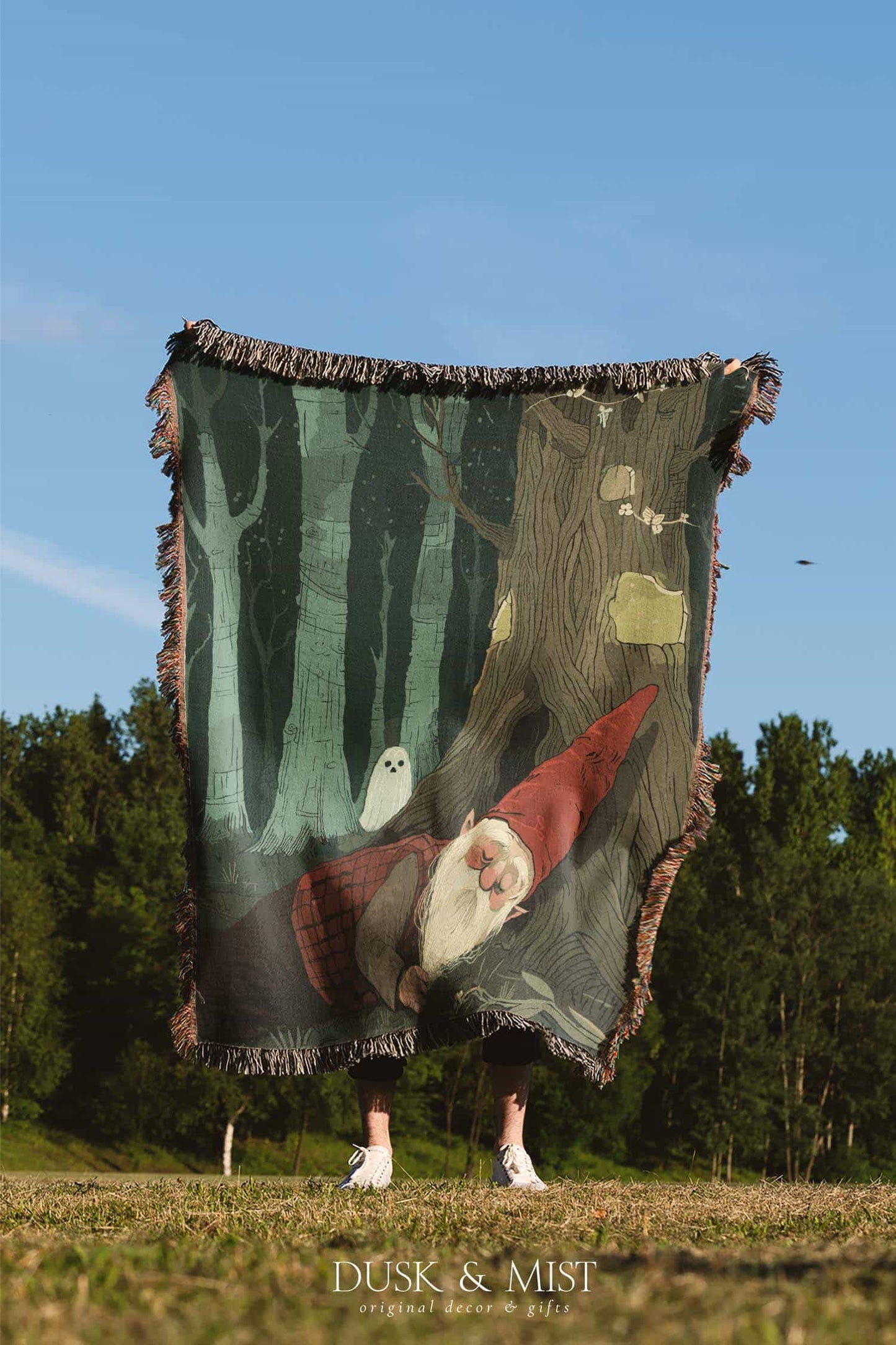 Woven cotton blanket depicting a sleeping gnome under a large tree, with a small ghost-like forest spirit in the background surrounded by dark green woods.