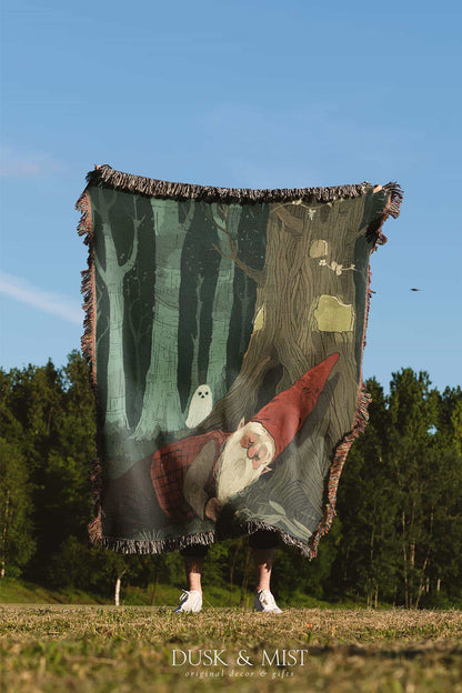 Woven cotton blanket depicting a sleeping gnome under a large tree, with a small ghost-like forest spirit in the background surrounded by dark green woods.