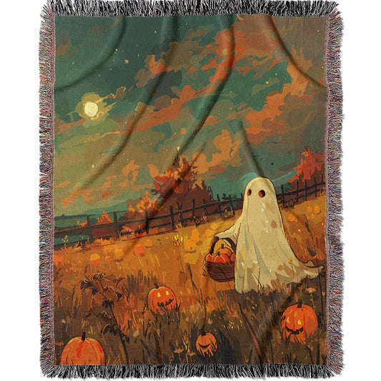 Woven cotton blanket depicting a ghost carrying a basket in a pumpkin-filled autumn field under a twilight sky.  
