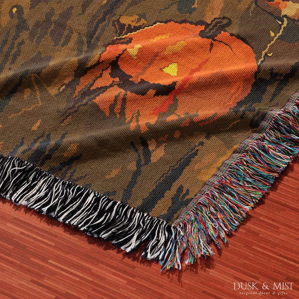 Woven cotton blanket depicting a ghost carrying a basket in a pumpkin-filled autumn field under a twilight sky.  