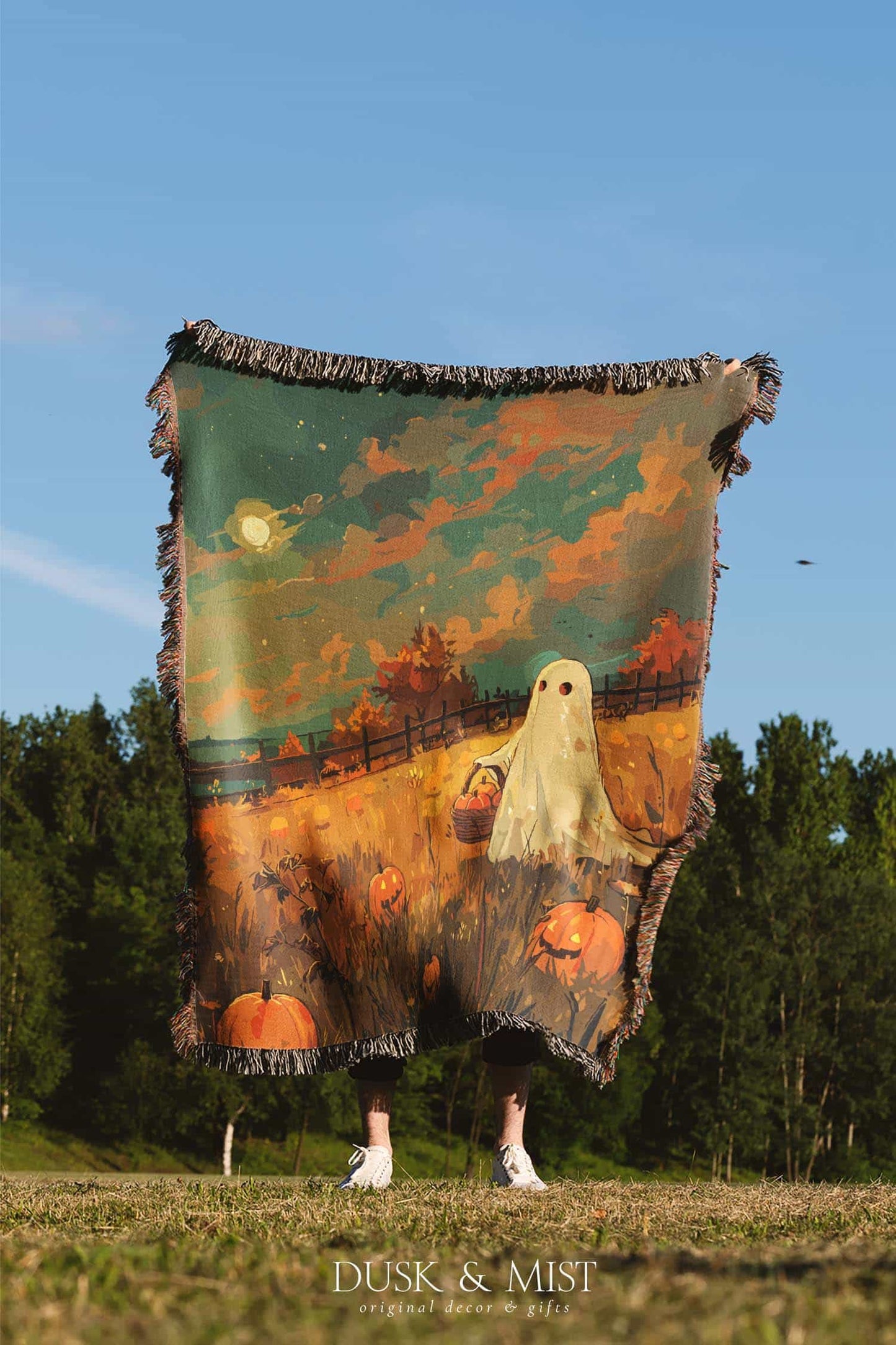 Woven cotton blanket depicting a ghost carrying a basket in a pumpkin-filled autumn field under a twilight sky.  