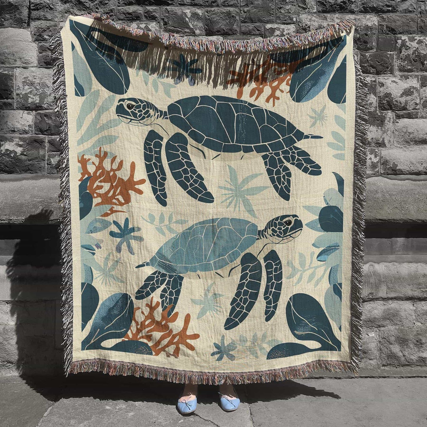 Woven cotton blanket featuring two sea turtles swimming among coral and aquatic plants, designed in teal, orange, and cream tones.  