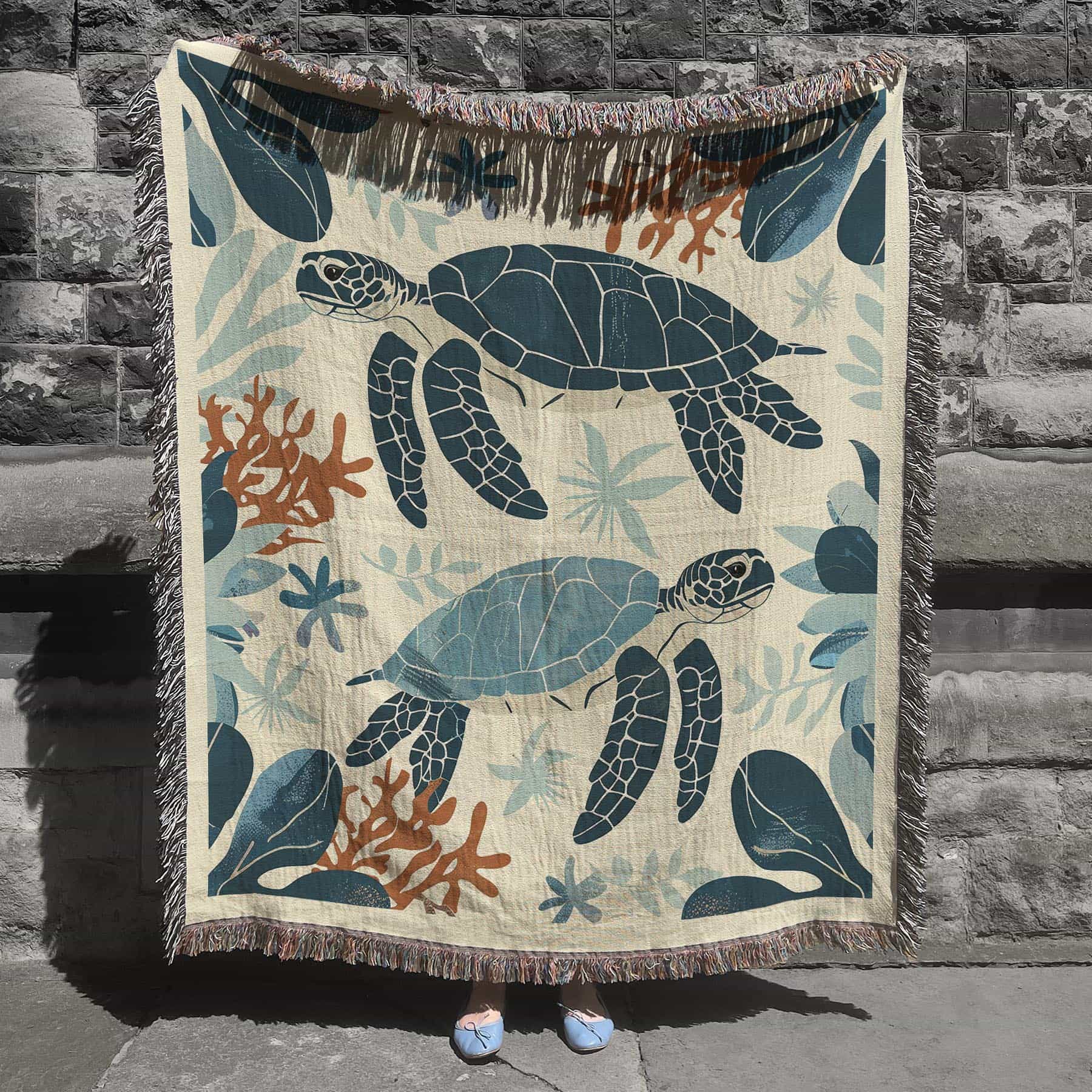 Woven cotton blanket featuring two sea turtles swimming among coral and aquatic plants, designed in teal, orange, and cream tones.  