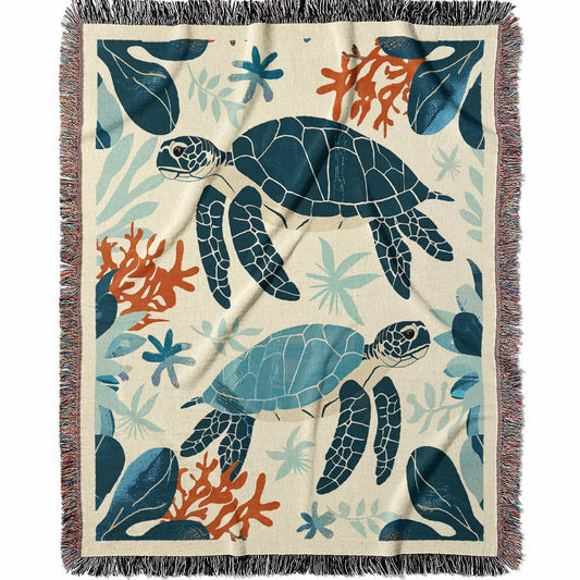 Woven cotton blanket featuring two sea turtles swimming among coral and aquatic plants, designed in teal, orange, and cream tones.  