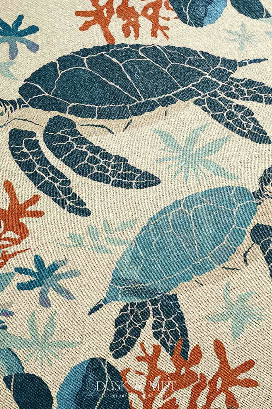 Woven cotton blanket featuring two sea turtles swimming among coral and aquatic plants, designed in teal, orange, and cream tones.  