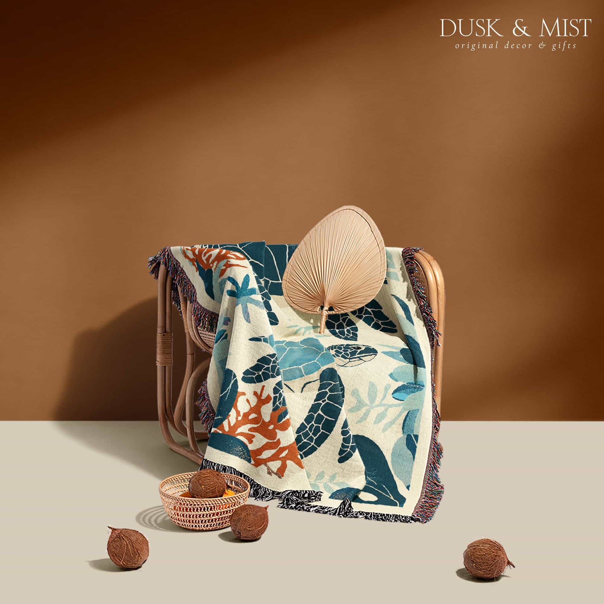 Woven cotton blanket featuring two sea turtles swimming among coral and aquatic plants, designed in teal, orange, and cream tones.  