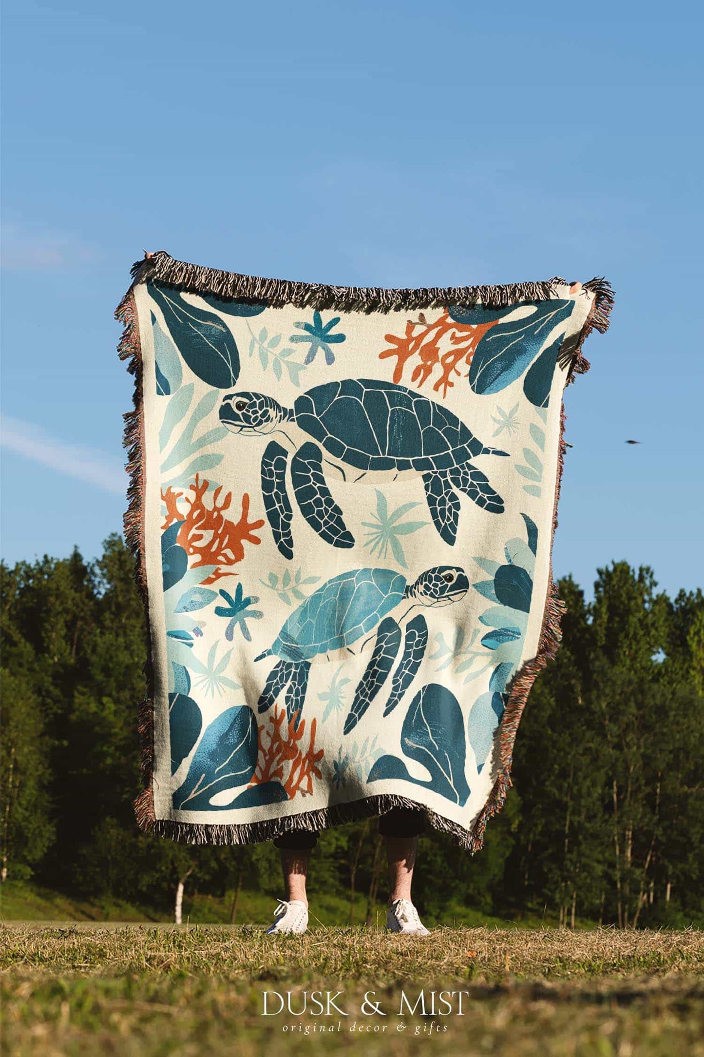 Woven cotton blanket featuring two sea turtles swimming among coral and aquatic plants, designed in teal, orange, and cream tones.  