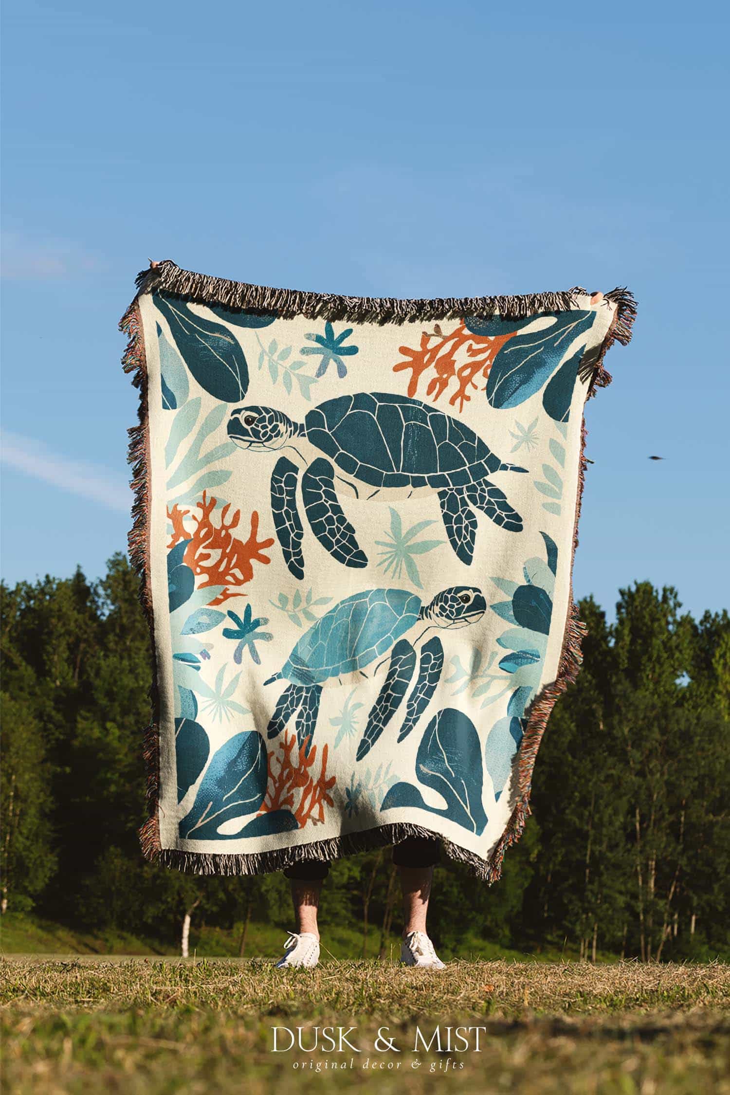 Woven cotton blanket featuring two sea turtles swimming among coral and aquatic plants, designed in teal, orange, and cream tones.  
