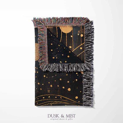 Woven cotton blanket featuring a profile of a woman with flowing hair illustrated as starry constellations, accented with golden moons and celestial motifs on a dark background.