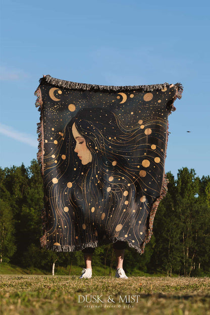 Woven cotton blanket featuring a profile of a woman with flowing hair illustrated as starry constellations, accented with golden moons and celestial motifs on a dark background.