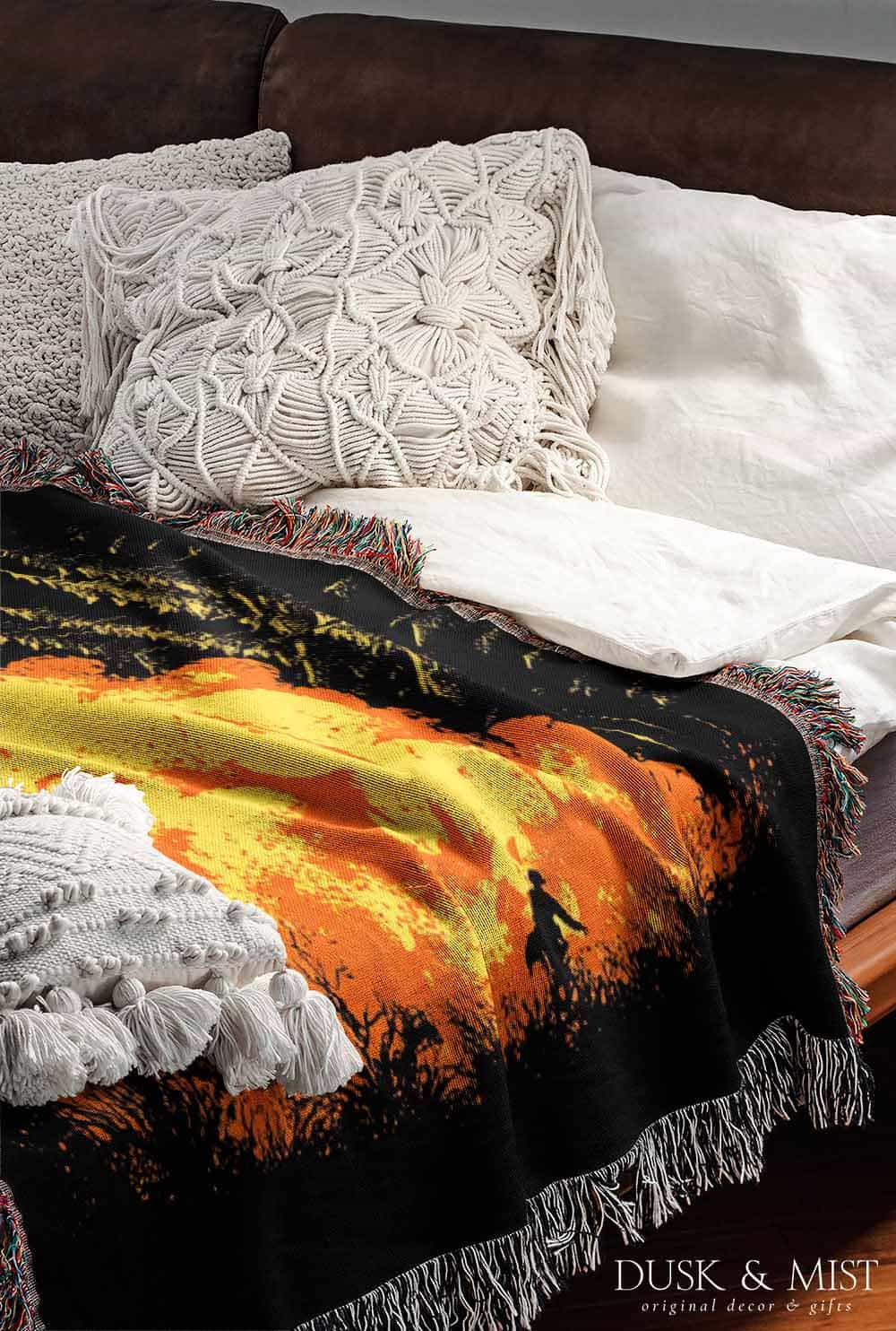 Woven cotton blanket featuring a UFO with a fiery orange beam blasting into a forest, with smoke clouds and a small human silhouette running at the bottom.