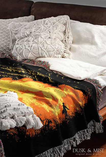 Woven cotton blanket featuring a UFO with a fiery orange beam blasting into a forest, with smoke clouds and a small human silhouette running at the bottom.