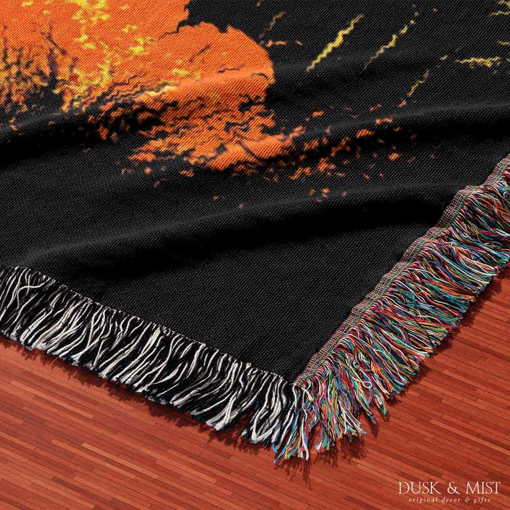 Woven cotton blanket featuring a UFO with a fiery orange beam blasting into a forest, with smoke clouds and a small human silhouette running at the bottom.
