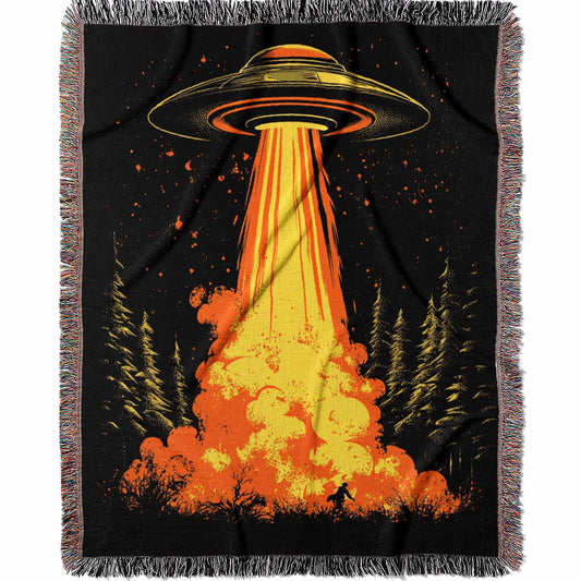 Woven cotton blanket featuring a UFO with a fiery orange beam blasting into a forest, with smoke clouds and a small human silhouette running at the bottom.