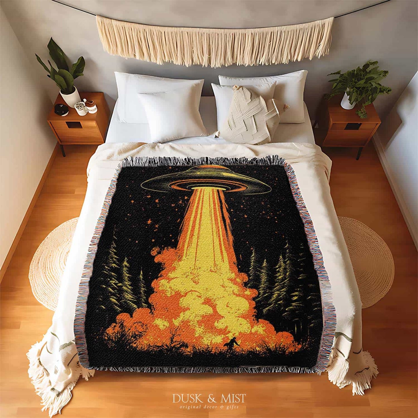 Woven cotton blanket featuring a UFO with a fiery orange beam blasting into a forest, with smoke clouds and a small human silhouette running at the bottom.