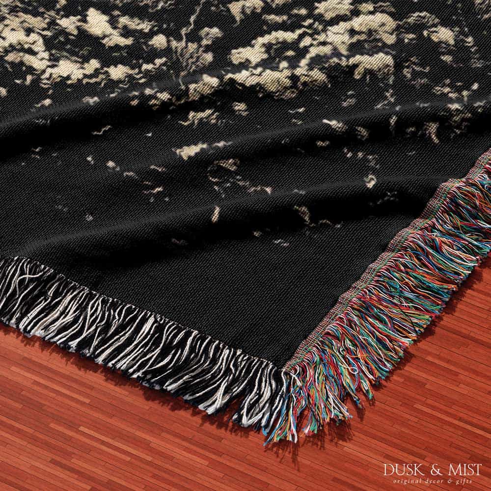 Woven cotton blanket featuring an alien and a human seated under a UFO’s glowing beam, reaching hands toward each other against a starry night sky.