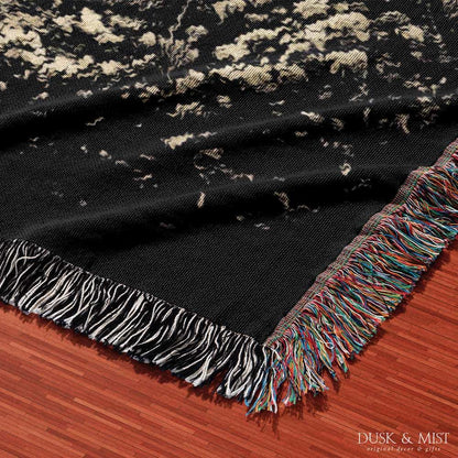 Woven cotton blanket featuring an alien and a human seated under a UFO’s glowing beam, reaching hands toward each other against a starry night sky.