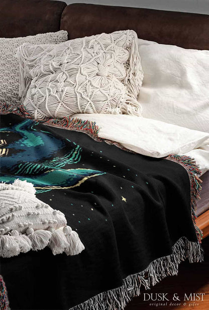 Woven cotton blanket featuring an astronaut riding a whale through space with colorful stars on a black background.
