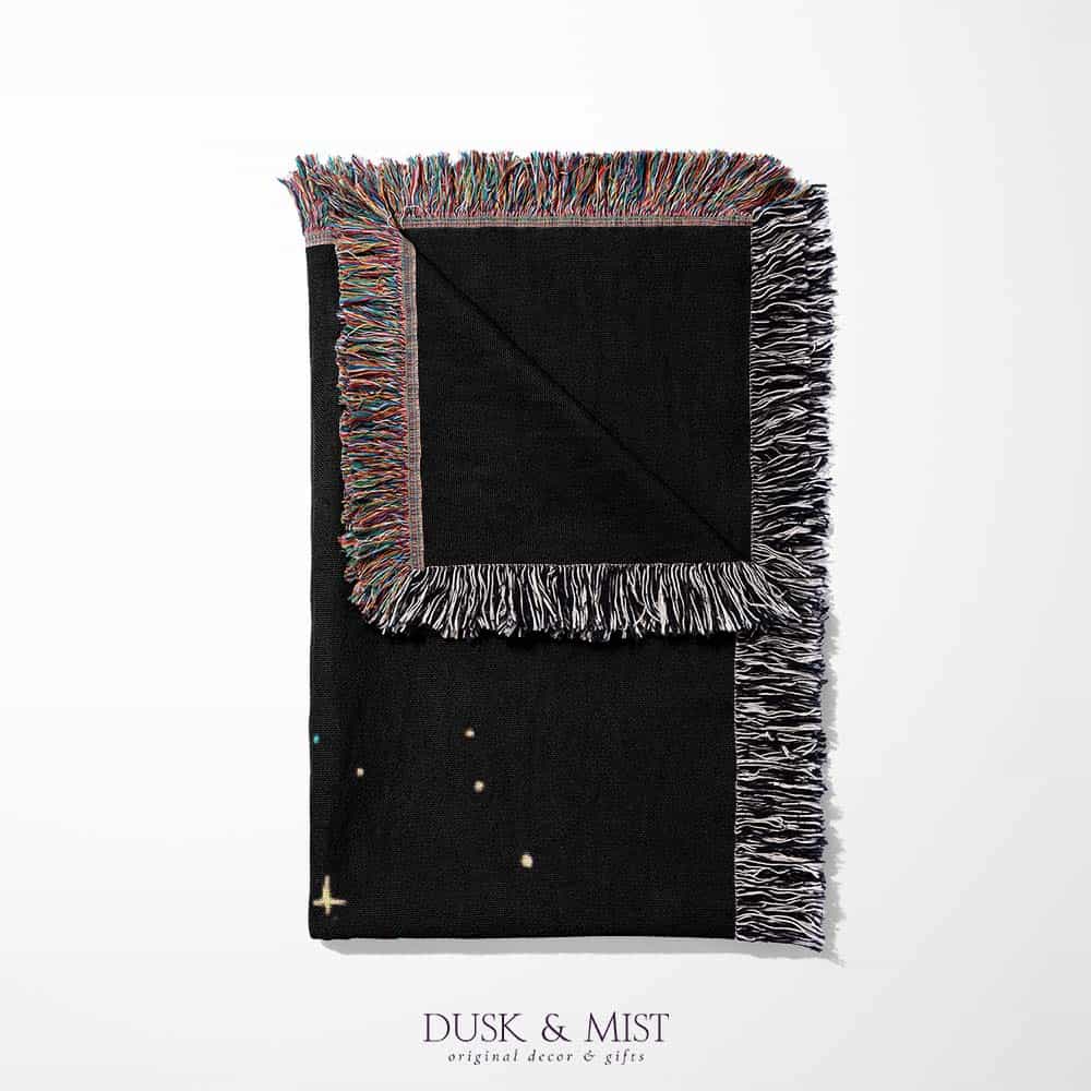 Woven cotton blanket featuring an astronaut riding a whale through space with colorful stars on a black background.