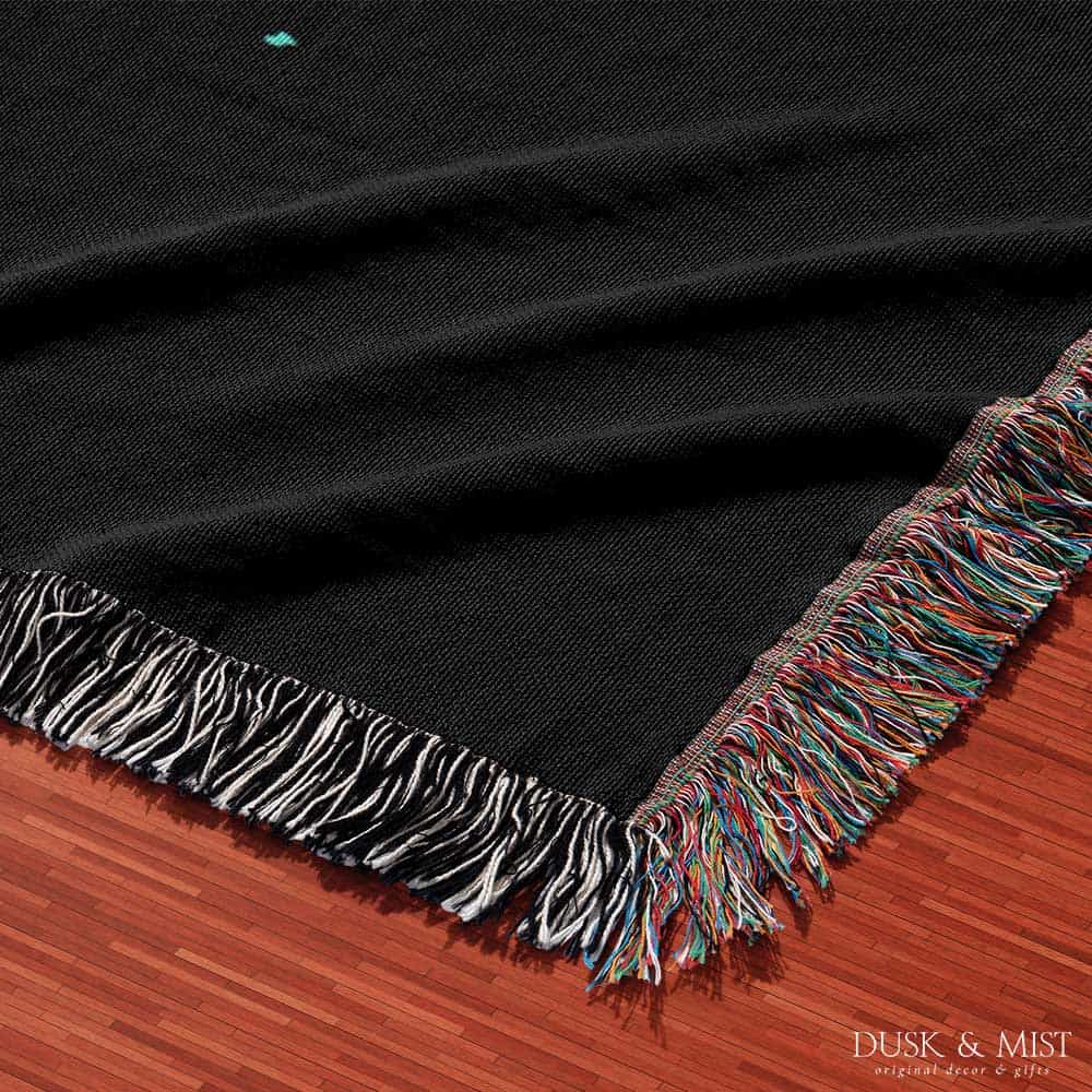 Woven cotton blanket featuring an astronaut riding a whale through space with colorful stars on a black background.