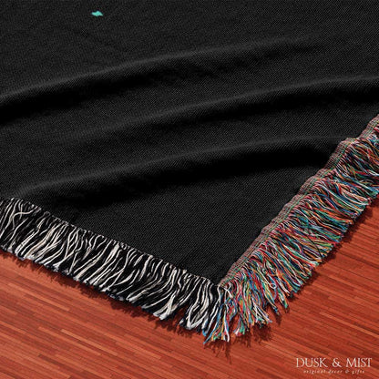 Woven cotton blanket featuring an astronaut riding a whale through space with colorful stars on a black background.