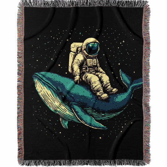 Woven cotton blanket featuring an astronaut riding a whale through space with colorful stars on a black background.