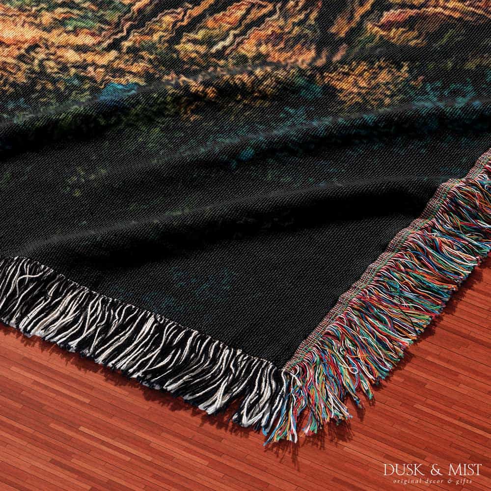 Woven cotton blanket showing a UFO beaming light onto a cow in a forest clearing under a starry night sky with trees and clouds.