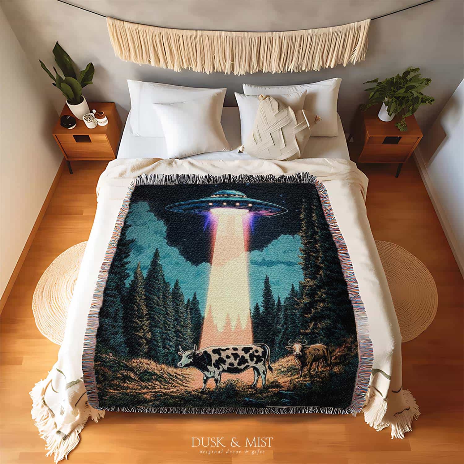 Woven cotton blanket showing a UFO beaming light onto a cow in a forest clearing under a starry night sky with trees and clouds.