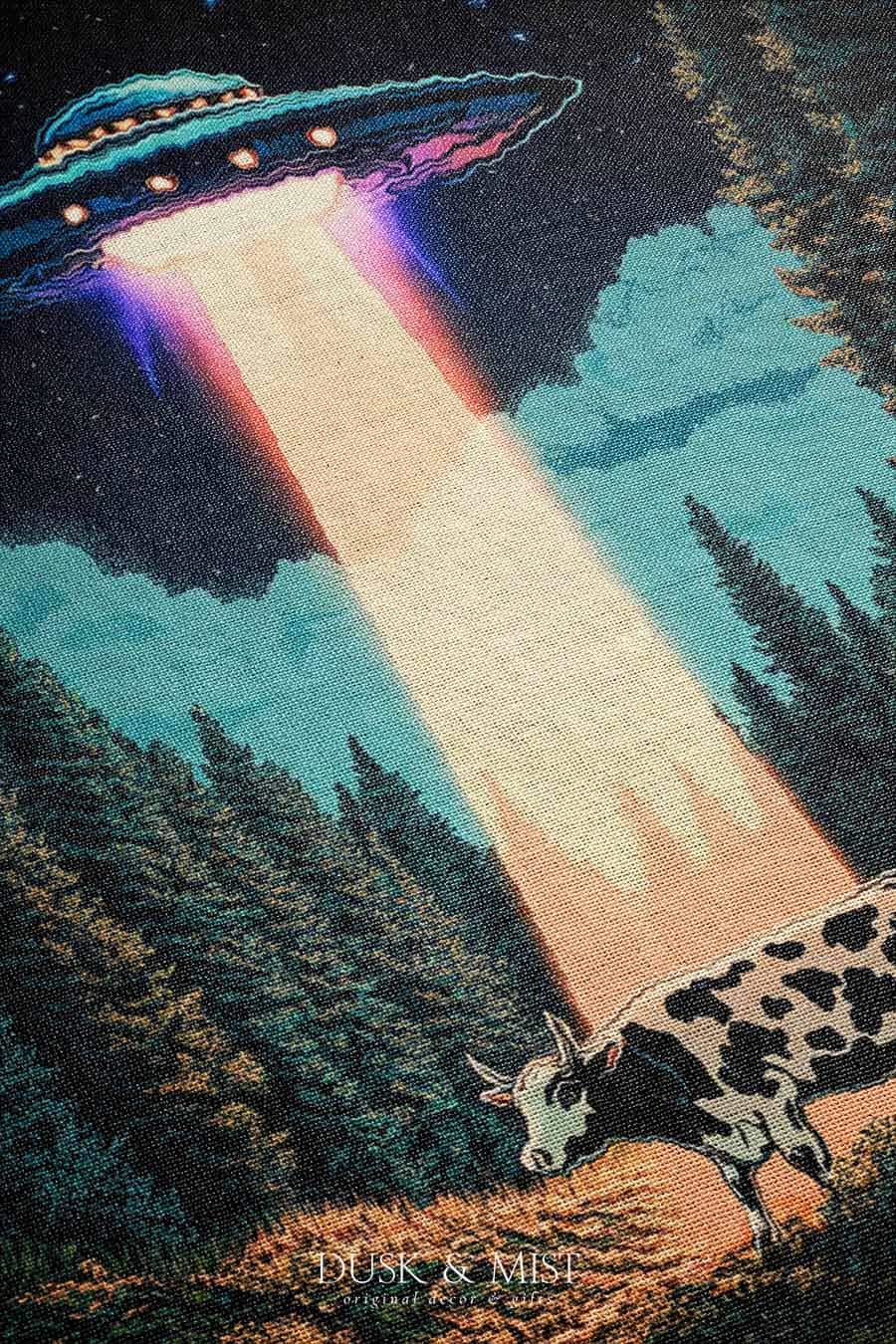 Woven cotton blanket showing a UFO beaming light onto a cow in a forest clearing under a starry night sky with trees and clouds.