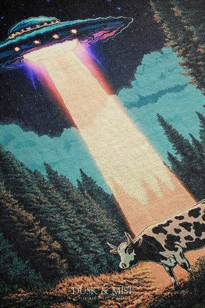 Woven cotton blanket showing a UFO beaming light onto a cow in a forest clearing under a starry night sky with trees and clouds.
