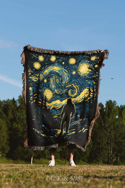 Woven cotton blanket featuring Bigfoot in silhouette against a Van Gogh-style starry night sky with swirling golden stars and dark forest trees.