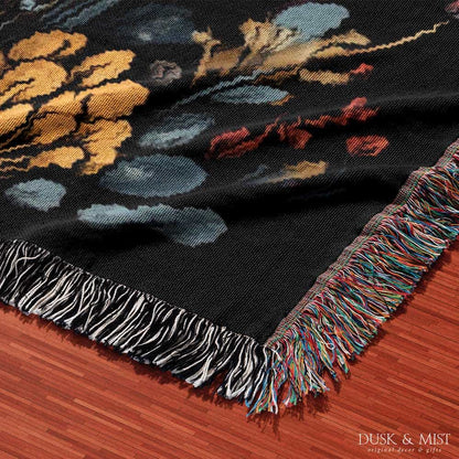 Woven cotton blanket featuring a botanical-style cluster of mushrooms in red, gold, and purple caps surrounded by plants and foliage on a black background.