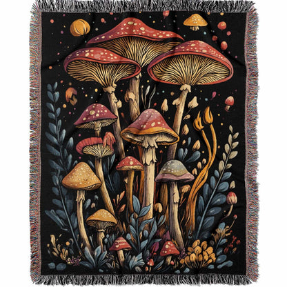 Woven cotton blanket featuring a botanical-style cluster of mushrooms in red, gold, and purple caps surrounded by plants and foliage on a black background.