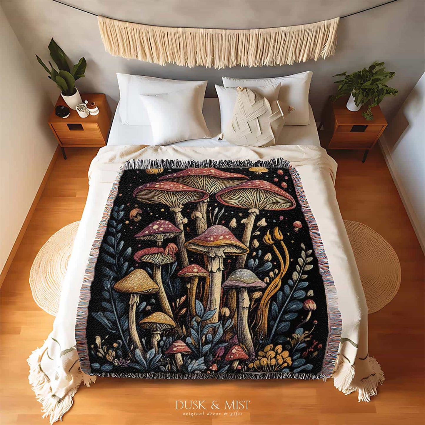 Woven cotton blanket featuring a botanical-style cluster of mushrooms in red, gold, and purple caps surrounded by plants and foliage on a black background.