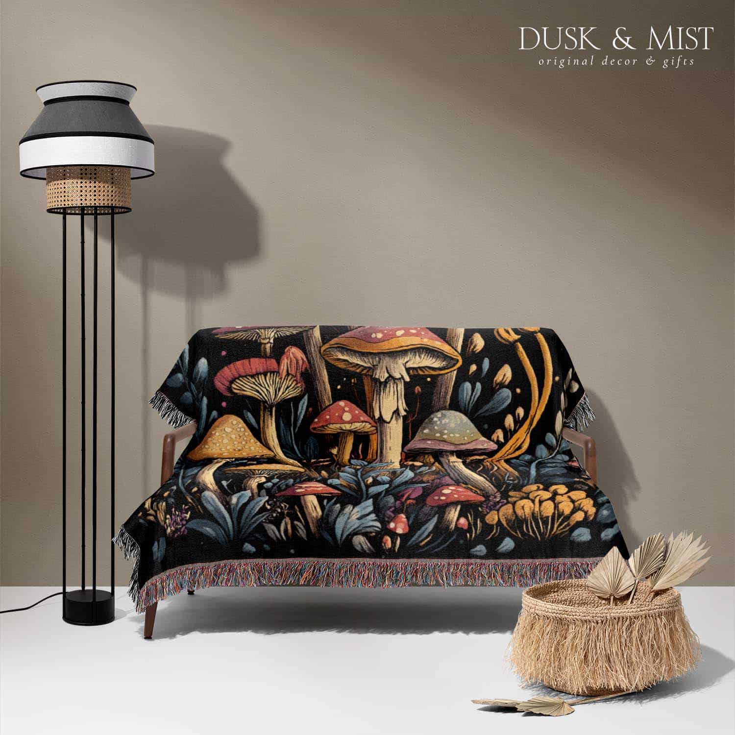 Woven cotton blanket featuring a botanical-style cluster of mushrooms in red, gold, and purple caps surrounded by plants and foliage on a black background.