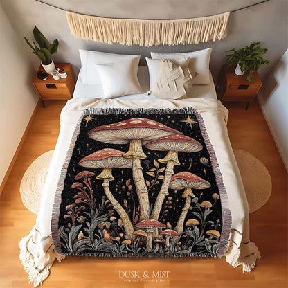 Woven cotton blanket featuring tall red-capped mushrooms under a starry sky with golden stars and surrounding plants on a black background.